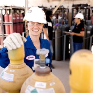 workers in hard hats and protective wear standing with groups of tall metal cylinders.