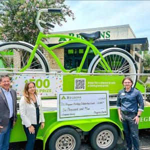 People stood in front of a large green bike on an event float with a cheque on the front 