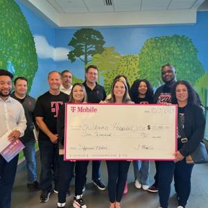 A group of people posed with a large check. A muraled wall behind them.