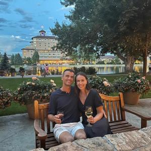 Christine Perkins and her husband seated in a beautiful garden holding a glass of wine.
