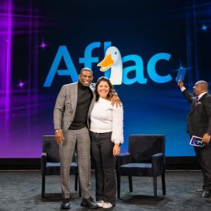 Coach Prime and Jaime Gaudet shown on stage with the Aflac logo.