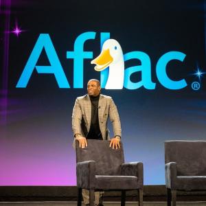 Coach Prime shown on stage with the Aflac logo.