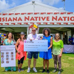 Five people posed with a large check and profiles of scholarship winners posed outside a booth "Louisiana Native Nations."
