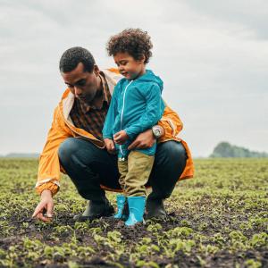 A father and son are shown looking at crops in a field.