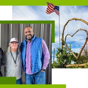 Three people with arms around each other. On the right A wooden heart hanging in an arch, an american flag on a pole next to it.