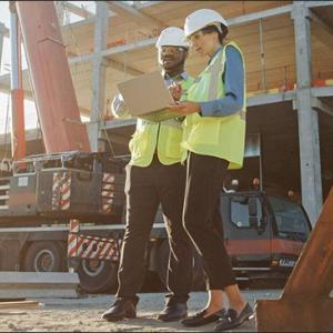 Two people looking at a laptop on a construction site.