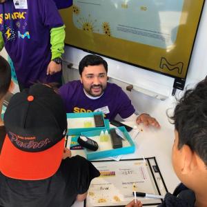 A SPARK employee kneels down over an experiment to talk to students. 