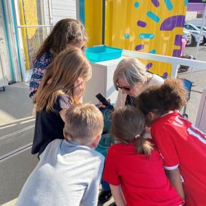 A woman is sitting while a group of students look over her at an experiment. 