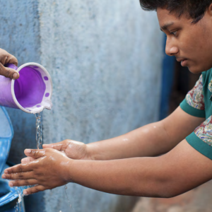 Young person having water poured over his hands so that they can wash them.
