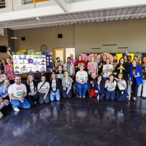 A group posed with a display. Many in matching rainbow shirts.