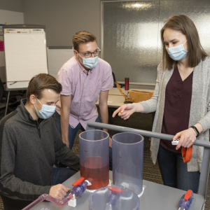 The model uses dyed water to simulate a pipeline cut and fill different tanks from a manifold.