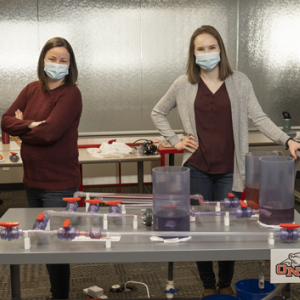 Pierce (left) and Loos (right), both graduates of ONU, pose with the ONU Model, a pipeline manifold connected to tankage.