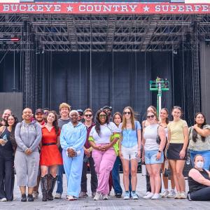 College program participants pose for a group photo in front of the main stage at Buckeye Country Superfest, standing on the festival grounds before the event begins.