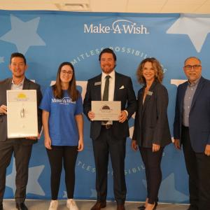 Five people standing and smiling in front of a blue background.