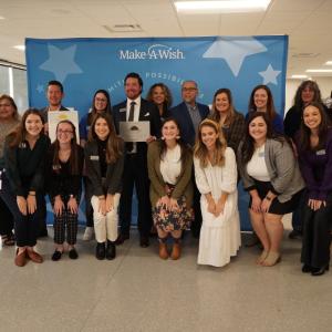 Large crowd of people stand in front of a blue background.