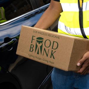A close-up of a volunteer in a safety vest holding a Los Angeles Regional Food Bank box.