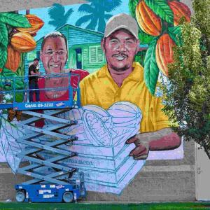 Artist Bobby Gaytan paints a mural of Francisco and Carlixta Martinez Contreras, sibling cocoa farmers from the Dominican Republic, outside Boise Co-op Market in Boise, ID.