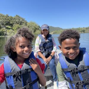 Danielle with her two children sitting in front of her in a boat on the water. All are wearing life vests.