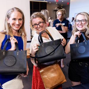 Three women holding black coach handbags