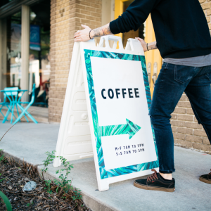 Person shown adjusting a sign in front of a coffee shop.