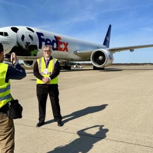 Dave Lange being photographed standing outside in front of a FedEx plane.