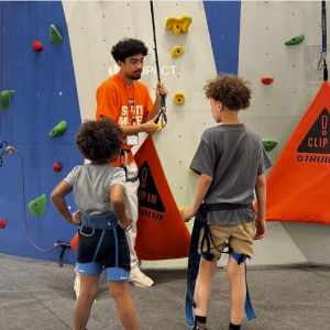 Two children about to be strapped in for a climbing wall adventure.