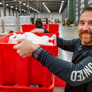 Person lifting up a red bin inside a warehouse building