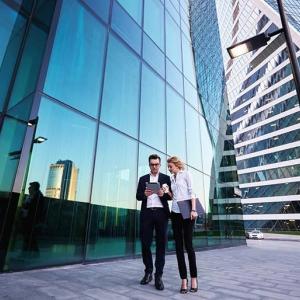 Two people looking at a tablet outside of a glass office building