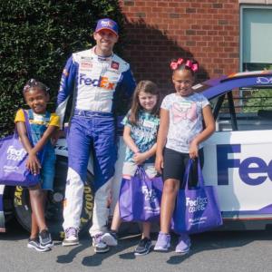 Denny Hamlin with children in front of a race car.