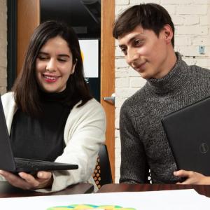 Two people seated at a desk and looking at a laptop