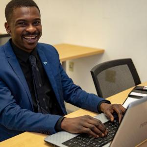 person smiling at camera while typing on laptop