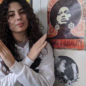 Woman standing next to a poster that reads Power & Equality, crossing her arms