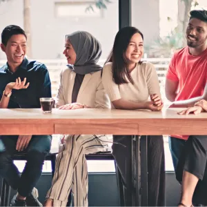 Group of six people seated at a table having coffee and smiling.