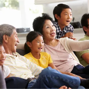 Asian family seated on a couch watching television.