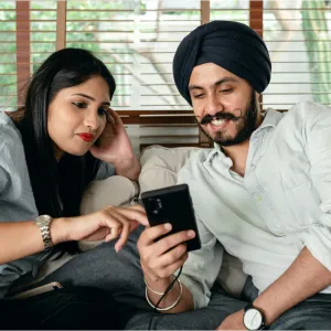 A couple seated on a couch looking at a smart phone. 