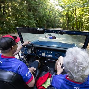 Gene and Donna Griffin driving in a jeep on a gravel path in the woods