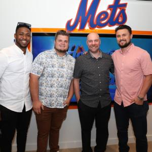 Group of four people standing in front of Mets logo