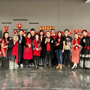 A group posed, many in matching red scarves. A display behind them.