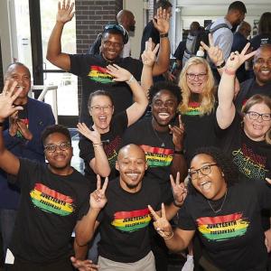 A group posed in matching "Juneteenth" shirts, giving peace-signs or raised hands.