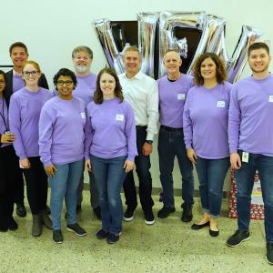 A group of people posed, most in matching purple shirts.