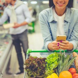 A couple shopping in a grocery store. One of them is consulting their phone.