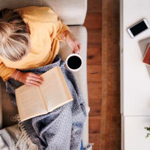 person reclining on a couch while reading and drinking coffee, seen from above