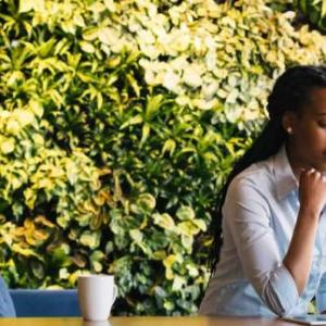 Two people looking at the same laptop computer. Another sits on a couch behind them using a device.