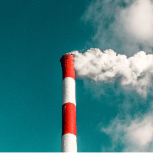 Red and white smokestack billowing smoke against a blue sky.