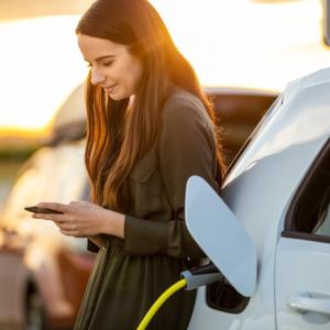 A person looking at their phone leaning on an EV plugged in.