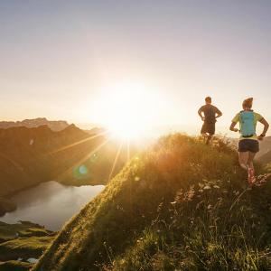 Photo of the sun setting with two people running on some hills 