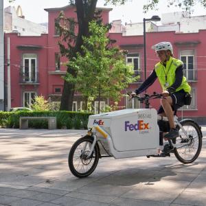 Person riding a FedEx bike outside with buildings and tree's behind them