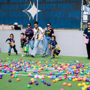 Children run across a turf field toward colorful eggs during a community egg hunt.