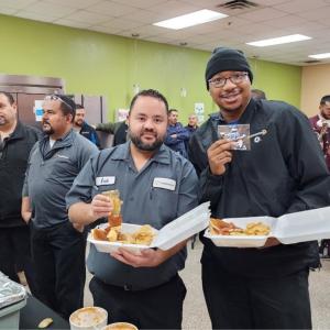 A roof full of employees, some in line for a buffet, two pose for the camera with containers of food.