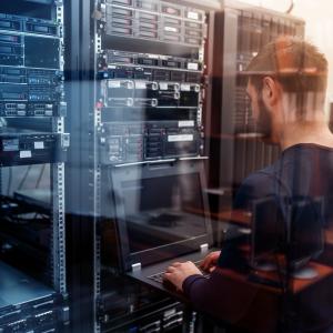 A person with a laptop working in a server room.